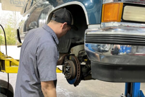 4 signs your car needs new brake rotors in Locust, NC. Image of Whitley Automotive mechanic working on worn brake rotors in shop on lifted truck.
