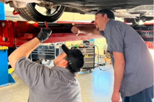 Suspension System Inspection in Locust, NC | Whitley Automotive. Mechanics at the shop performing a suspension system inspection on car on lift in shop using flashlight.