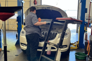 Preventative Maintenance Services near me in Locust, NC at Whitley Automotive. Image of a white Volkswagen sedan with open hood and a technician using the dipstick of the car to check the oil level in preparation for preventative maintenance service.