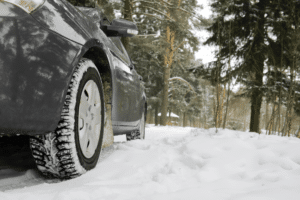 Winter car maintenance services in Marshville, NC with Whitley Automotive. Image of black car's tires driving on a snow covered road.