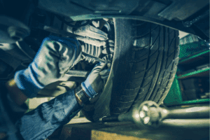steering and tires, auto repair in Locust, NC at Whitley Automotive. Close-up of a mechanic's gloved hands working on a vehicle’s suspension and wheel assembly under the car.