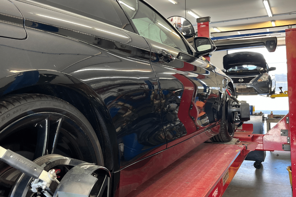 steering works, auto repair in Locust, NC at Whitley Automotive. Image of a black BMW on a red Hunter alignment rack with sensors attached, showcasing precision wheel alignment in a well-lit auto repair shop.