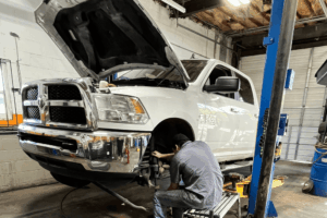 Car inspection, auto repair in Locust, NC by Whitley Automotive. Image of a RAM 2500 lifted in a repair bay with a technician working on the front suspension and brakes for reliable business vehicle uptime.